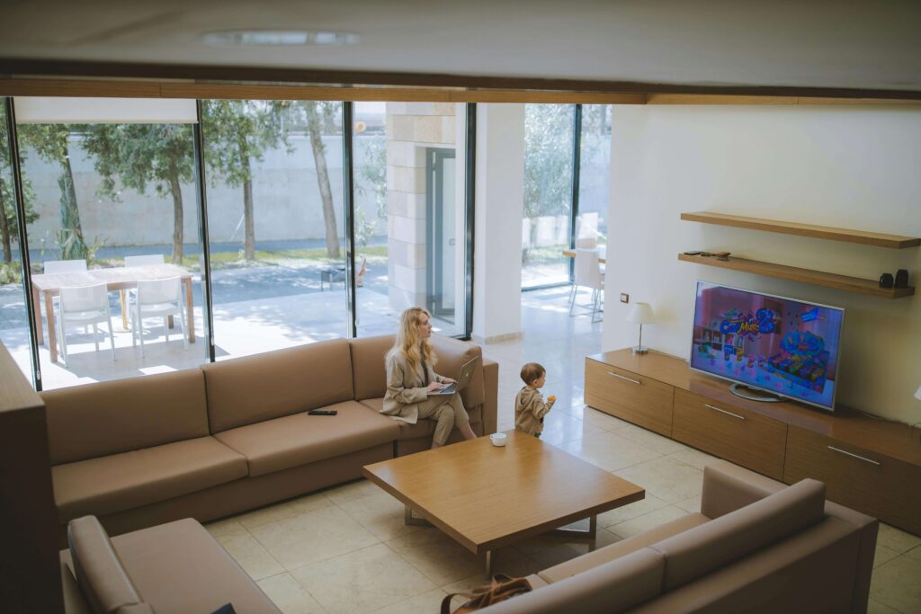 Woman and her son watching their favourite TV channel in a spacious living room, while the woman also holds a laptop on her lap.