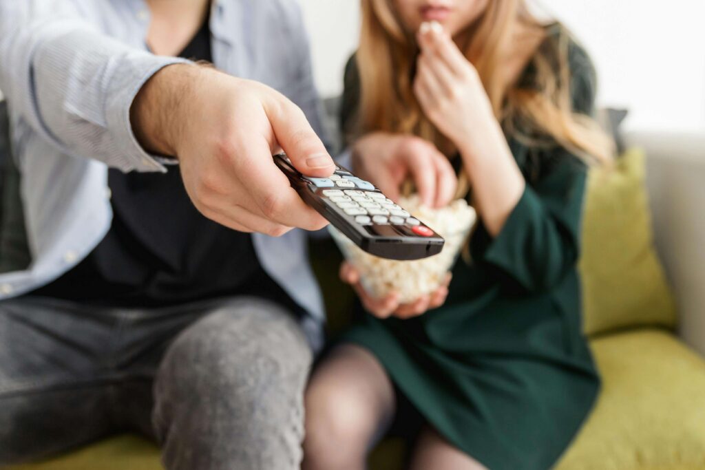 A man and his blonde partner watching TV together while eating popcorn.