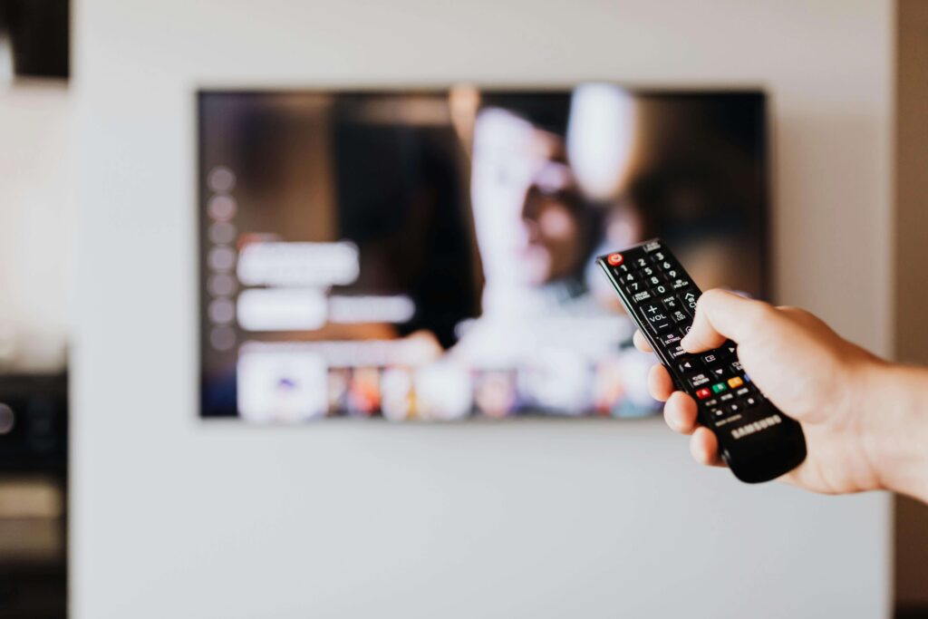 man lounging while holding the TV remote control — he seems about to change the channel or turn up the volume.