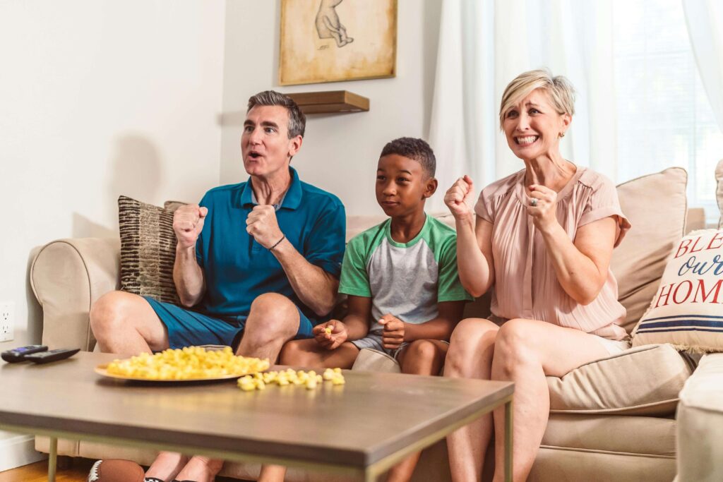 A family consisting of a man, a blonde woman, and a Black child who appears to be adopted. They are enjoying popcorn and seem to be watching a match together