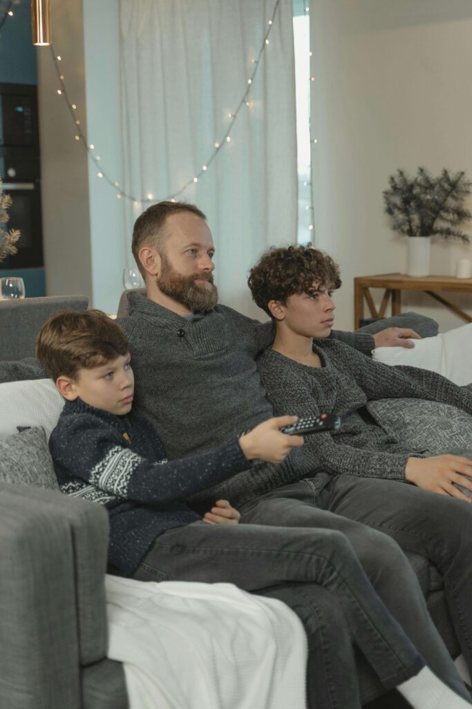 Blond man and his two children watching TV with focused expressions, suggesting they are engaged in something important or watching a movie.